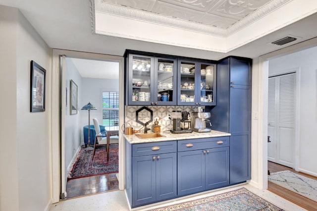 bar with blue cabinetry, a raised ceiling, decorative backsplash, and light hardwood / wood-style flooring