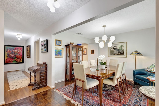 dining room with dark parquet floors, a textured ceiling, and a notable chandelier