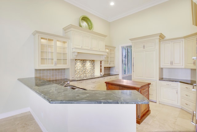 kitchen featuring sink, decorative backsplash, a towering ceiling, ornamental molding, and kitchen peninsula