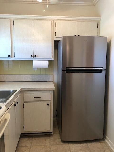 kitchen featuring stainless steel fridge, backsplash, white stove, light tile patterned flooring, and sink