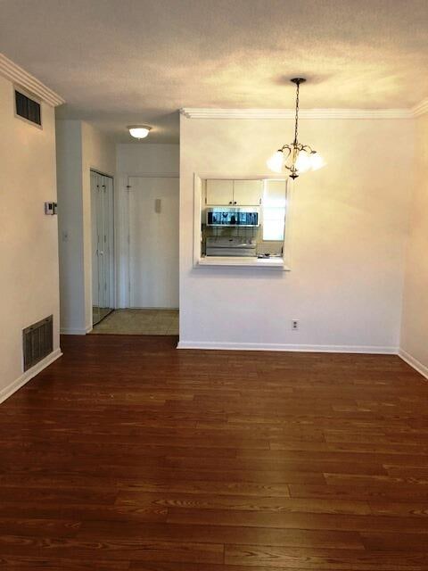 unfurnished living room with dark wood-type flooring, ornamental molding, and an inviting chandelier