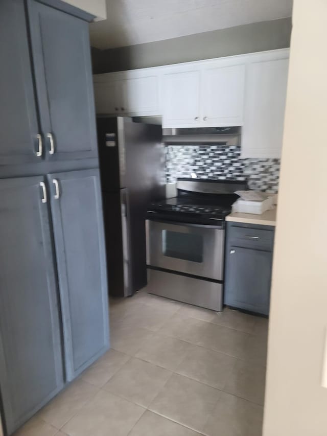 kitchen with gray cabinetry, backsplash, white cabinets, light tile patterned floors, and appliances with stainless steel finishes