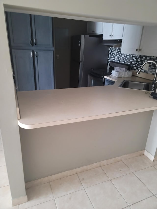 kitchen with white cabinets, tasteful backsplash, light tile patterned floors, stainless steel range, and sink