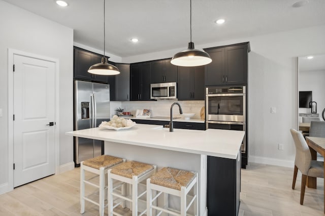 kitchen with appliances with stainless steel finishes, hanging light fixtures, light hardwood / wood-style flooring, and an island with sink