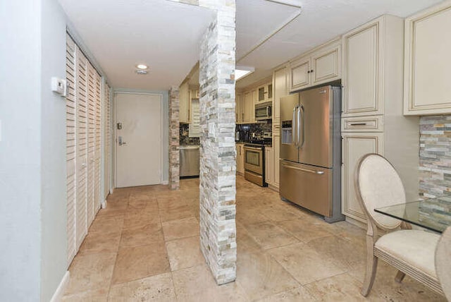 kitchen featuring cream cabinets, decorative backsplash, stainless steel appliances, and ornate columns