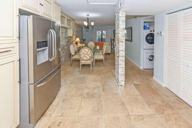 kitchen featuring stainless steel refrigerator with ice dispenser, stacked washer / drying machine, ornate columns, an inviting chandelier, and hanging light fixtures