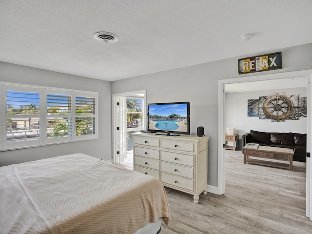 bedroom with a textured ceiling, multiple windows, and light wood-type flooring