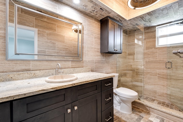 bathroom with vanity, toilet, tile walls, and a shower with door