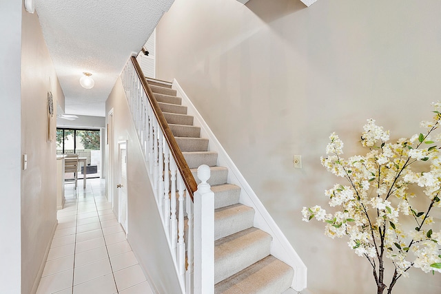 stairway with a textured ceiling and tile patterned flooring