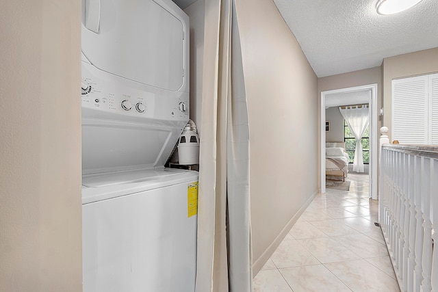 clothes washing area featuring stacked washer / dryer, a textured ceiling, and light tile patterned flooring