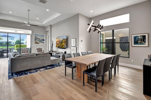 dining space featuring a towering ceiling, light wood-type flooring, and ceiling fan with notable chandelier