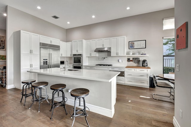 kitchen with appliances with stainless steel finishes, white cabinetry, a kitchen bar, and an island with sink