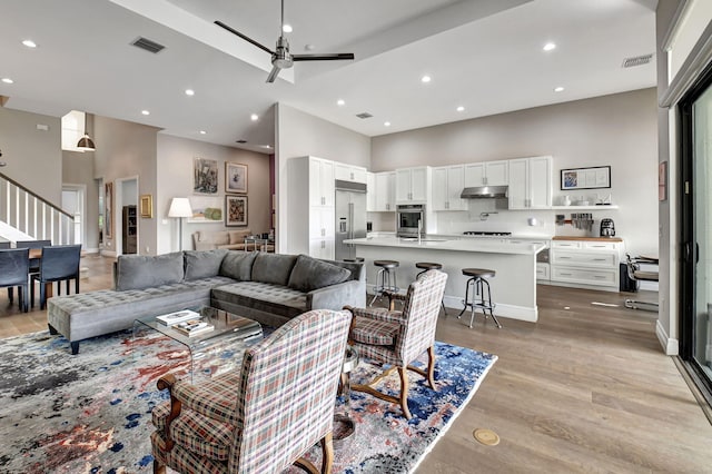 living room featuring light hardwood / wood-style floors, a high ceiling, and ceiling fan