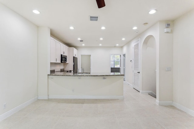 kitchen featuring light stone counters, white cabinets, kitchen peninsula, light tile patterned floors, and appliances with stainless steel finishes