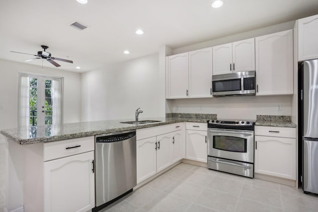 kitchen featuring stainless steel appliances, light stone counters, kitchen peninsula, sink, and white cabinetry