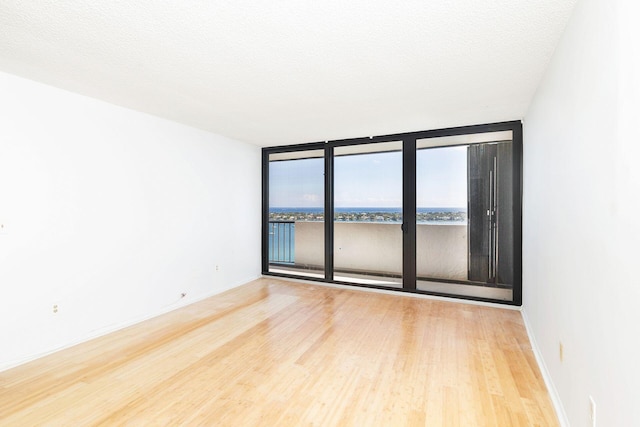 empty room featuring floor to ceiling windows, a textured ceiling, a water view, and hardwood / wood-style flooring