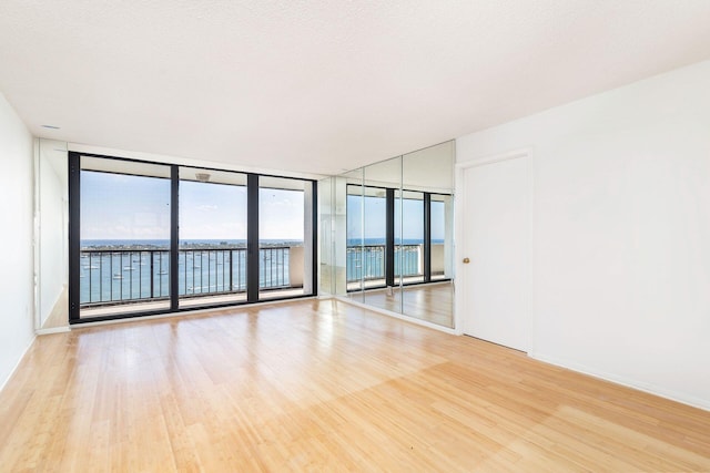 unfurnished room featuring a textured ceiling, light wood-type flooring, a water view, and expansive windows