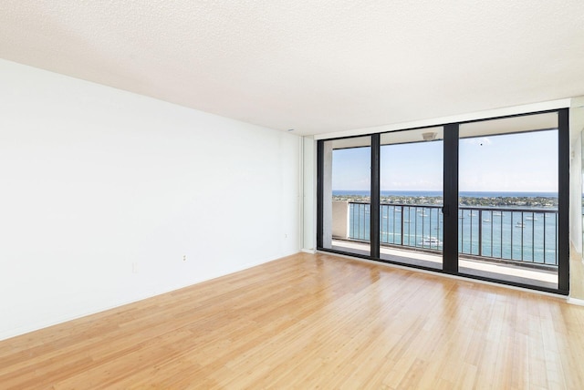 unfurnished room featuring expansive windows, light hardwood / wood-style flooring, a water view, and a textured ceiling