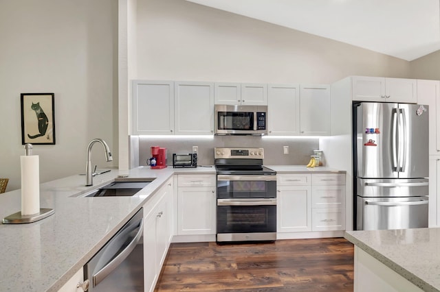 kitchen with appliances with stainless steel finishes, lofted ceiling, white cabinets, and light stone countertops