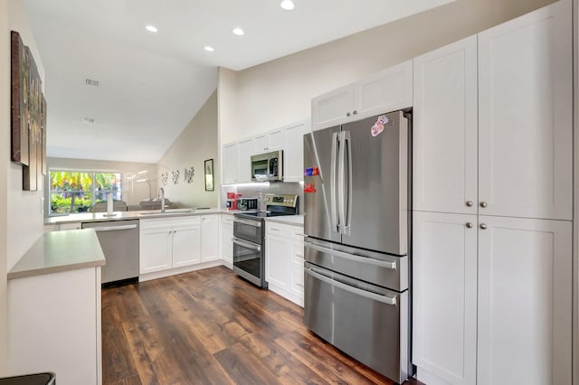 kitchen with appliances with stainless steel finishes, sink, white cabinetry, vaulted ceiling, and dark wood-type flooring