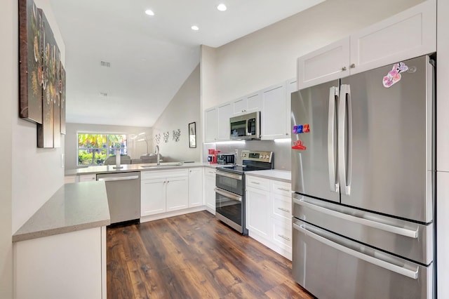 kitchen featuring lofted ceiling, white cabinets, kitchen peninsula, appliances with stainless steel finishes, and dark hardwood / wood-style floors