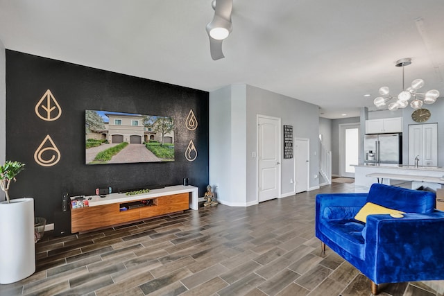 living room featuring dark wood-type flooring, ceiling fan with notable chandelier, and sink