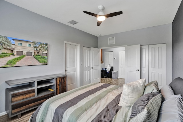 bedroom with multiple closets, hardwood / wood-style flooring, and ceiling fan