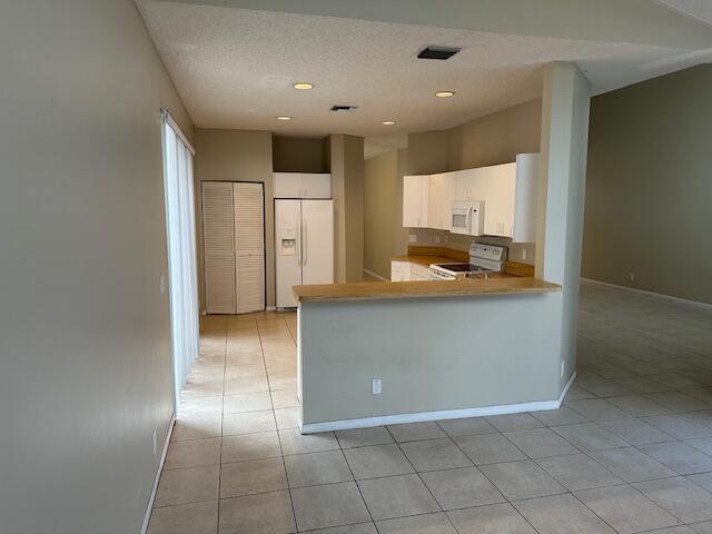 kitchen with white appliances, a textured ceiling, kitchen peninsula, white cabinetry, and light tile patterned floors