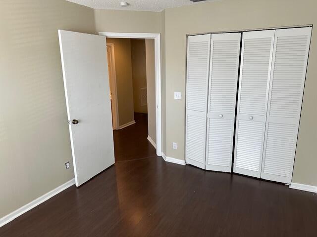 unfurnished bedroom with dark wood-type flooring, a textured ceiling, and a closet