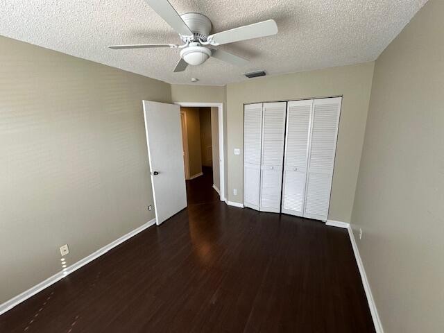 unfurnished bedroom featuring a closet, ceiling fan, a textured ceiling, and dark hardwood / wood-style floors