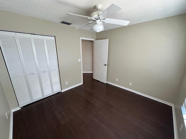 unfurnished bedroom with a closet, a textured ceiling, ceiling fan, and dark hardwood / wood-style flooring