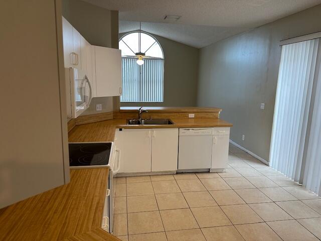 kitchen with lofted ceiling, sink, light tile patterned floors, white cabinetry, and white appliances