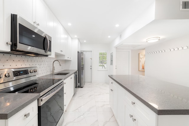 kitchen featuring appliances with stainless steel finishes, white cabinets, sink, and dark stone counters