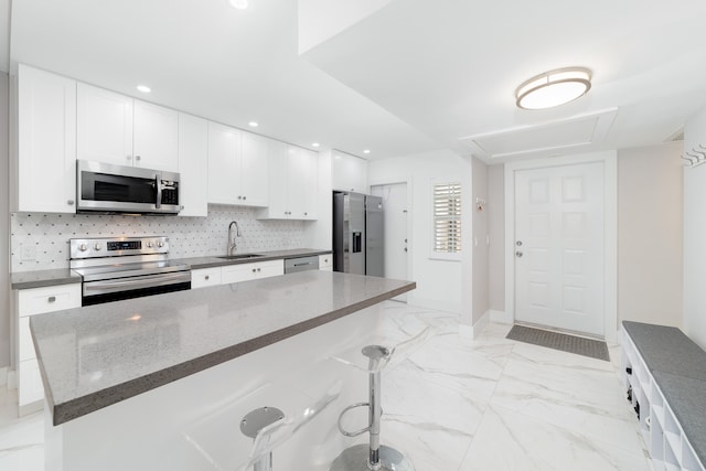 kitchen featuring appliances with stainless steel finishes, sink, dark stone counters, white cabinets, and a breakfast bar