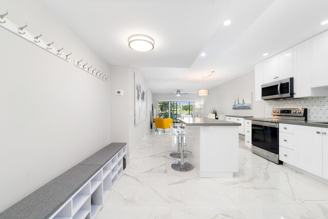 kitchen with a kitchen island, a breakfast bar, white cabinetry, decorative light fixtures, and stainless steel appliances