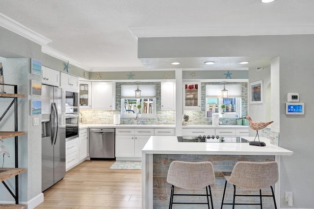 kitchen with light hardwood / wood-style flooring, white cabinetry, ornamental molding, a breakfast bar area, and stainless steel appliances