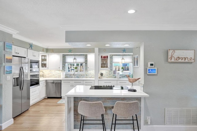 kitchen with a kitchen bar, light wood-type flooring, stainless steel appliances, and white cabinetry