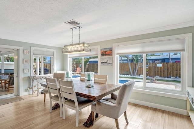 dining space featuring crown molding, light wood-type flooring, and a textured ceiling