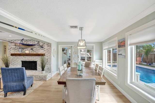 dining room featuring a fireplace, a textured ceiling, light hardwood / wood-style floors, and crown molding