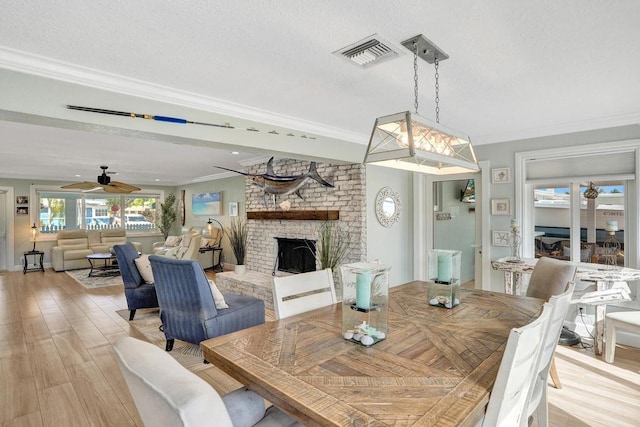 dining area with ceiling fan, a brick fireplace, light hardwood / wood-style flooring, crown molding, and a textured ceiling