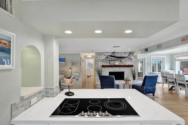 kitchen featuring light stone countertops, black electric stovetop, a brick fireplace, crown molding, and light hardwood / wood-style floors