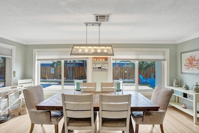 dining room featuring crown molding, light wood-type flooring, and a textured ceiling