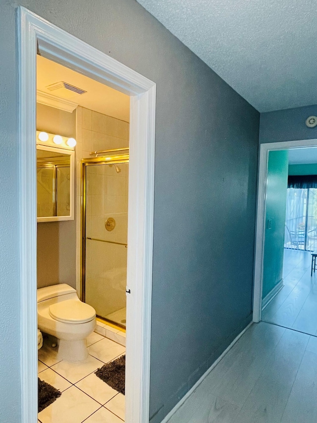 bathroom with a textured ceiling, toilet, walk in shower, and tile patterned floors