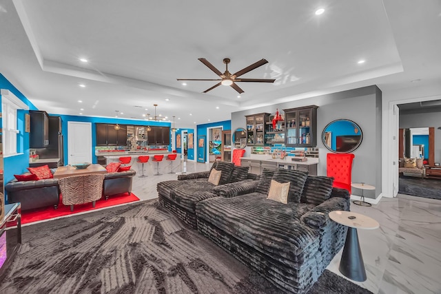 living room featuring ceiling fan with notable chandelier and a raised ceiling