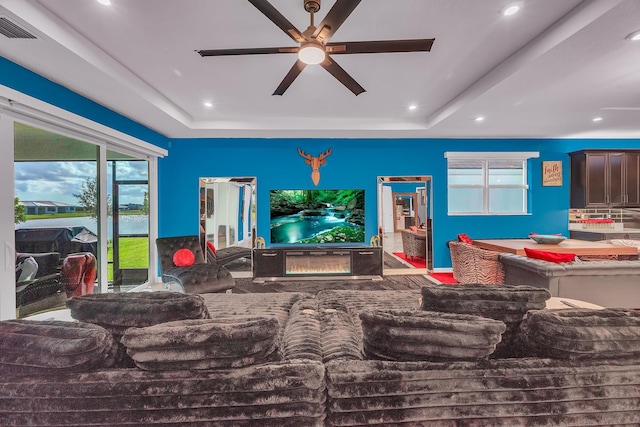 living room with a healthy amount of sunlight, ceiling fan, and a raised ceiling