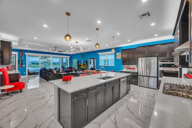 kitchen with hanging light fixtures, a center island with sink, ceiling fan, sink, and stainless steel appliances