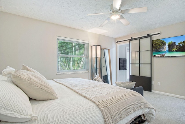 carpeted bedroom featuring a barn door, ceiling fan, and a textured ceiling