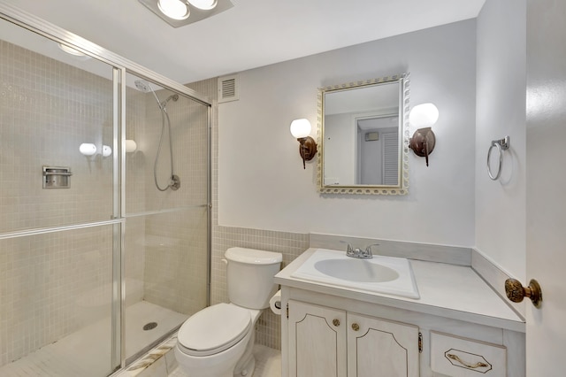 bathroom featuring vanity, toilet, tile walls, and a shower with shower door