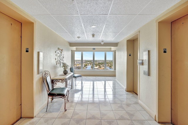 hall with a paneled ceiling, elevator, and light tile patterned floors