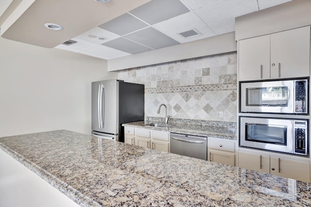 kitchen featuring light stone countertops, sink, a drop ceiling, backsplash, and stainless steel appliances